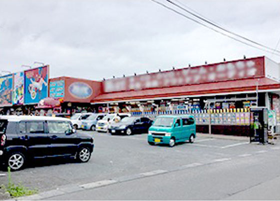 写真：車が複数台駐車スペースがある店舗、1階建のお店の上部に赤い外壁塗装がされています。